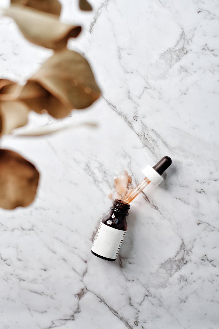 Glass serum bottle with pipette on a marble surface, ideal for skincare and beauty concepts.