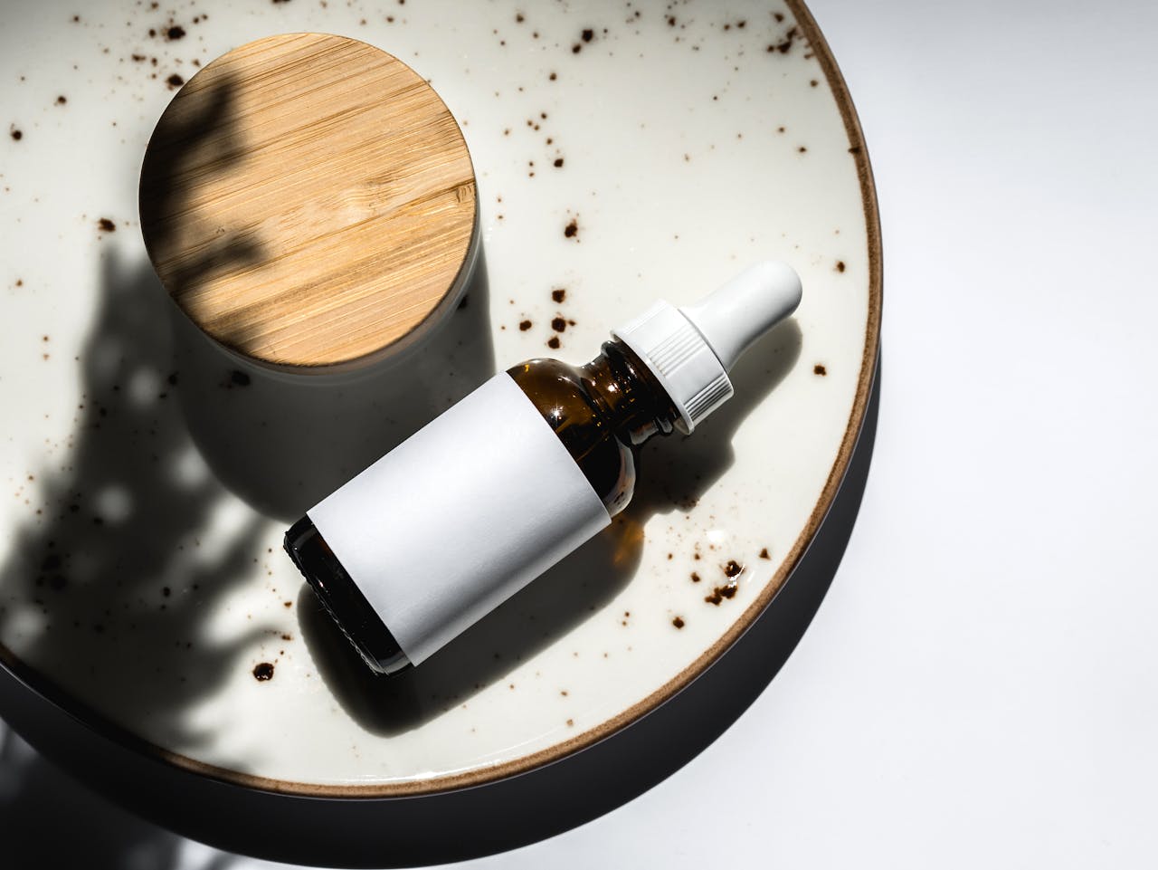 Elegant flatlay of a skincare essential dropper bottle on a ceramic plate. Perfect for product branding and beauty blogs.
